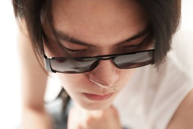 Kendine güvenen ve şık bir Asyalı beyaz duvarın üzerinde güneş gözlüğü takıyor. - Evet. Yüksek kalite fotoğraf.