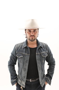 Beyaz duvarın üzerinde kot ceket ve fötr şapka giyen sakallı genç adam. Yüksek kalite fotoğraf.