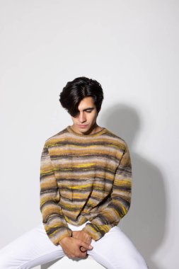 Siyah saçlı, beyaz arka planda poz veren yakışıklı bir genç. Dikey. Yüksek kalite fotoğraf.