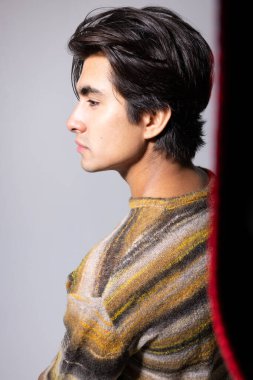 Siyah saçlı beyaz arka planda poz veren genç bir adamın yan portresi. Dikey. Yüksek kalite fotoğraf.