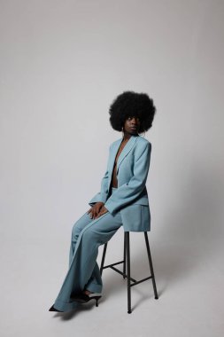 Mavi takım elbise giyen afro saçlı neşeli bir kadının stüdyo portresi. Dikey. Yüksek kalite fotoğraf.