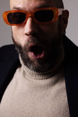 Sakallı, güneş gözlüğü takan, güvenli bir şekilde içeride poz veren olgun kel bir adam. Yüksek kalite fotoğraf.