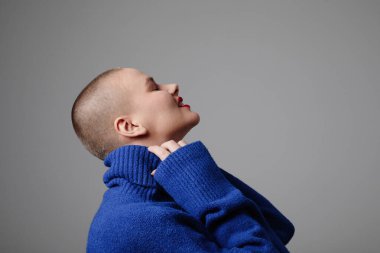 İçerde poz veren, günlük mavi süveter giyen mutlu genç kel kadın. İzole edilmiş. Yüksek kalite fotoğraf.