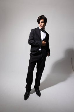 Beyaz arka planda poz veren zarif siyah takım elbiseli yakışıklı bir genç. Yüksek kalite fotoğraf.