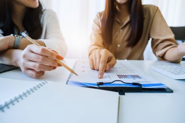 Müzakere, Analiz, Tartışma, Asyalı kadın ekonomist ve pazarlamacı, şirketin risk ve zararlarını önlemek için yatırım planlama amaçlı bir mali veri tablosuna işaret ediyorlar.