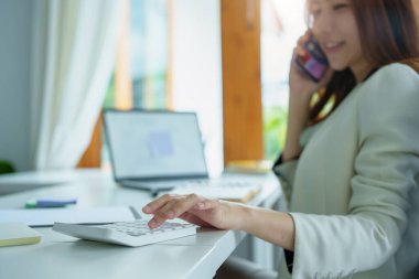 Çalışmak için finansal bütçe hesap makinesi, not defteri, telefon ve bilgisayar kullanan Asyalı bir banka çalışanının portresi.