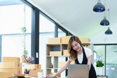 Çevrimiçi pazarlama paketi ve KOBİ teslimat kavramının neşeli başarısı ile bilgisayar laptopu kullanarak gülümseyen bağımsız Asyalı kadının küçük işletme girişimciliğini başlatan.