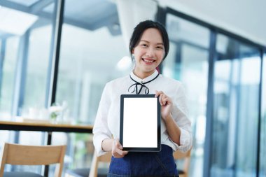Küçük bir işletme kuran ve açan genç bir Asyalı kadın, elinde tablet tutan gülümseyen bir yüz ile bir kahve dükkanının önünde duruyor. İş sahibi, restoran, kafe konsepti.