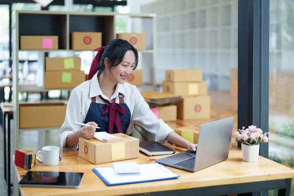 stock image Starting small business entrepreneur of independent Asian woman smiling using computer laptop with cheerful success of online marketing package box items and SME delivery concept.