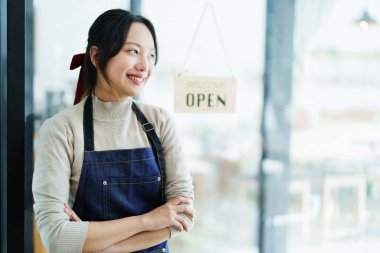 Küçük bir işletme kuran ve açan genç bir Asyalı kadın, kafeterya tezgahının önünde duran önlüklü gülen bir yüz gösteriyor. İş sahibi, Restoran, Barista, Cafe, Çevrimiçi KOBİ.