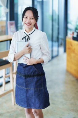 Küçük bir işletme kuran ve açan genç bir Asyalı kadın, elinde tablet tutan gülümseyen bir yüz ile bir kahve dükkanının önünde duruyor. İş sahibi, restoran, kafe konsepti.