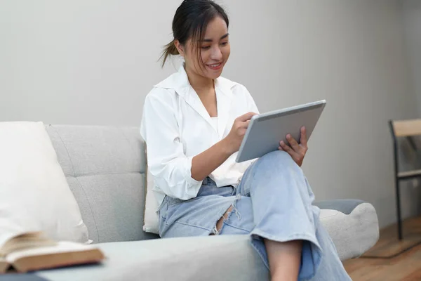 一个年轻的亚洲女人坐在沙发上使用平板电脑的肖像 — 图库照片
