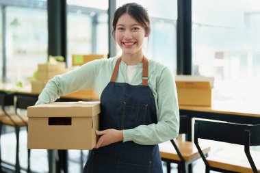 Portrait of a small startup Asian female entrepreneur SME owner picking up a yellow shirt before packing it in an inner box with a customer. Online Business Ideas and Freelance.