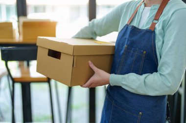 Portrait of a small startup Asian female entrepreneur SME owner picking up a yellow shirt before packing it in an inner box with a customer. Online Business Ideas and Freelance.