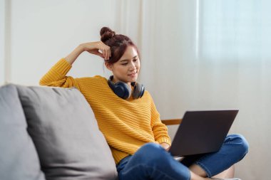 Kanepede bilgisayar kullanan Asyalı genç bir kadının portresi..