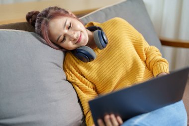 Kanepede bilgisayar kullanan Asyalı genç bir kadının portresi..