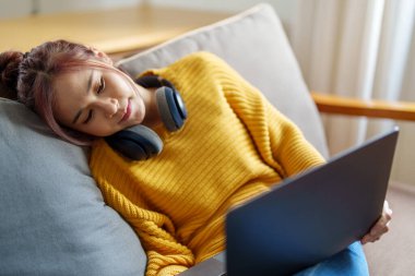 Kanepede bilgisayar kullanan Asyalı genç bir kadının portresi..