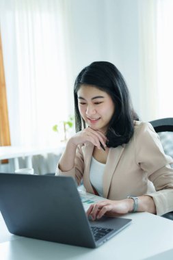 Düşünceli bir Asyalı iş kadınının portresi finansal tablolara bakıyor ve masasındaki bilgisayarı kullanarak pazarlama planları yapıyor..