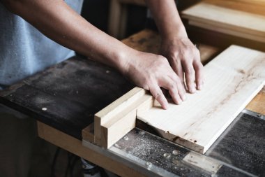 Woodworking practitioners use saw blades to cut wood pieces to assemble and build wooden tables for their clients
