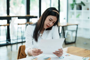 Masasındaki telefon ve mali belgeleri kullanırken stresli yüzünü gösteren güzel bir Asyalı kadın çalışanın portresi..