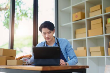 Küçük bir girişimin resmi ve KME sahibi, Asyalı bir girişimci müşteriler için iç kutulara paketlemeden önce ürünleri organize etme talimatlarını kontrol ediyor.