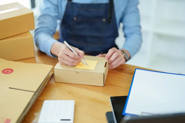 stock image small startup, and SME owner, an Asian male entrepreneur, is writing down information on a notepad to organize the product before packing it into the inner box for the customer.