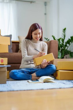 Küçük bir girişimin portresi, bir KME sahibi, bir Asyalı bayan girişimci ürünleri müşterilerle birlikte iç kutulara koymadan önce ürünleri düzenlemek için siparişleri kontrol ediyor. Serbest kavramlar.