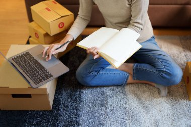 Küçük bir girişimin portresi, bir KME sahibi, bir Asyalı bayan girişimci ürünleri müşterilerle birlikte iç kutulara koymadan önce ürünleri düzenlemek için siparişleri kontrol ediyor. Serbest kavramlar.