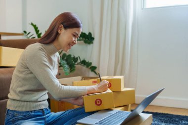 Küçük bir girişimin portresi, bir KME sahibi, bir Asyalı bayan girişimci ürünleri müşterilerle birlikte iç kutulara koymadan önce ürünleri düzenlemek için siparişleri kontrol ediyor. Serbest kavramlar.