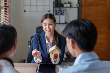 Bir emlakçının portresi kontratı imzaladıktan sonra bir çift için anahtarlı bir ev modelliği yapıyor..