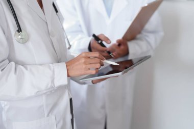 Tedavi öncesi hasta sorunlarını tartışmak için tablet kullanan Asyalı bir kadın doktor ve erkek doktorun portresi.