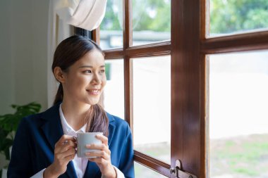 Asyalı bir iş kadınının portresi. Mola sırasında elinde bir fincan kahveyle gülen bir yüz gösteriyor..