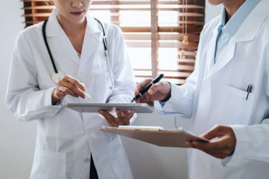 Tedavi öncesi hasta sorunlarını tartışmak için tablet kullanan Asyalı bir kadın doktor ve erkek doktorun portresi.
