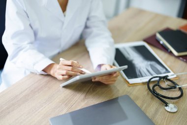 Asyalı bir kadın doktor, tedavi öncesi hasta semptomlarını analiz etmek için tablet bilgisayar kullanıyor..