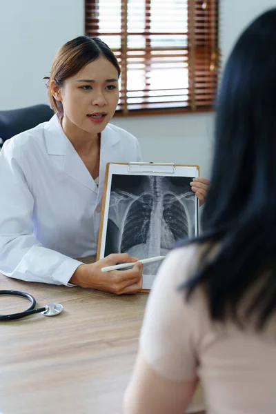 Азиатская Женщина Врач Указывает Рентгеновскую Пленку Пациента Объяснить Процесс Лечения — стоковое фото
