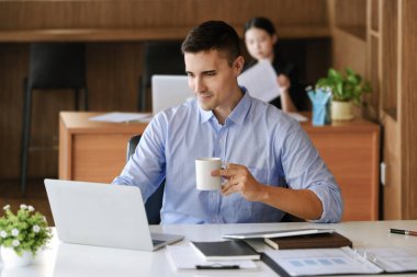 Erkek pazarlama yöneticileri bilgisayar, iPad ve pazarlama analiz kağıtları kullanmadan önce uykusuzluğu azaltmak için çalışırken kahve içerler.