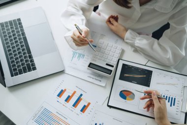 Müzakere, Analiz, Tartışma, Asyalı kadın ekonomist ve pazarlamacı, şirketin risk ve zararlarını önlemek için yatırım planlama amaçlı bir mali veri tablosuna işaret ediyorlar.
