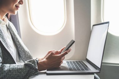 Başarılı bir Asyalı iş kadını ya da resmi takım elbiseli kadın girişimci uçuş sırasında akıllı telefon ve bilgisayar kullanarak birinci sınıf bir koltukta oturur..