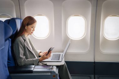Başarılı bir Asyalı iş kadını ya da resmi takım elbiseli kadın girişimci birinci sınıf koltukta oturur ve uçuş sırasında bilgisayarlı bir belge kullanır..