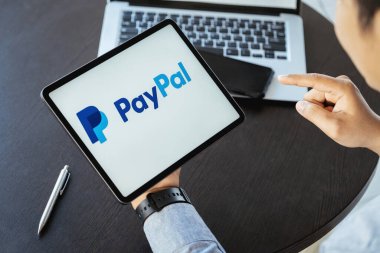 CHIANG MAI, THAILAND - 28 NOV 2021: PayPal uygulamalarıyla el ele tutuşan adam ekranda. PayPal bir çevrimiçi elektronik ödeme sistemidir.