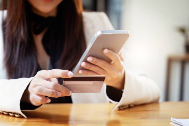 İnternetten alışveriş yapmak için cep telefonu ve kredi kartı kullanan Asyalı genç bir kadın..