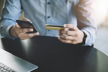 Çevrimiçi Alışveriş ve İnternet Ödemeleri, Asyalı adam internet üzerinden alışveriş yapmak veya dijital dünyada ayak işleri yapmak için kredi kartı ve cep telefonlarını kullanıyor