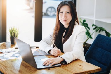 Bir kadın girişimci ya da iş kadını, ahşap bir masada çalışırken gülen bir yüz gösteriyor.
