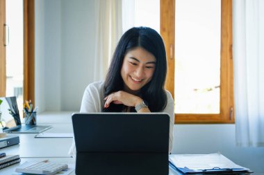 Bir kadın girişimci ya da iş kadını, ahşap bir masa üzerinde çalışan bir tablet bilgisayarı kullanarak gülen bir yüz gösteriyor.