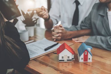 Banka memuru, eşiyle konuşan emlak çalışanı, ofisteki ev kredisi faiz oranları, kredi, sigorta, mali risk yönetimi kavramları hakkında Tablet bilgisayarında bilgi edinin.