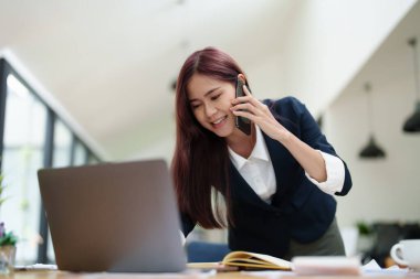 Asyalı iş kadını iş ortağıyla görüşmek için telefonu kullanıyor..