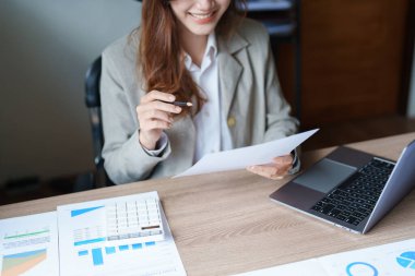 Düşünceli bir Asyalı iş kadınının portresi finansal tablolara bakıyor ve masasındaki bilgisayarı kullanarak pazarlama planları yapıyor..