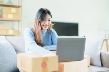 Çevrimiçi pazarlama paketi ve KOBİ teslimat kavramının neşeli başarısı ile bilgisayar laptopu kullanarak gülümseyen bağımsız Asyalı kadının küçük işletme girişimciliğini başlatan.