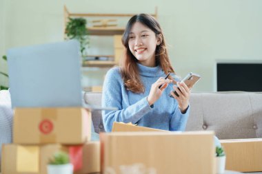 Çevrimiçi pazarlama paketi ve KOBİ teslimat kavramının neşeli başarısı ile bilgisayar laptopu kullanarak gülümseyen bağımsız Asyalı kadının küçük işletme girişimciliğini başlatan.