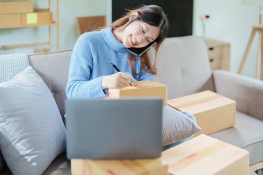Çevrimiçi pazarlama paketi ve KOBİ teslimat kavramının neşeli başarısı ile bilgisayar laptopu kullanarak gülümseyen bağımsız Asyalı kadının küçük işletme girişimciliğini başlatan.